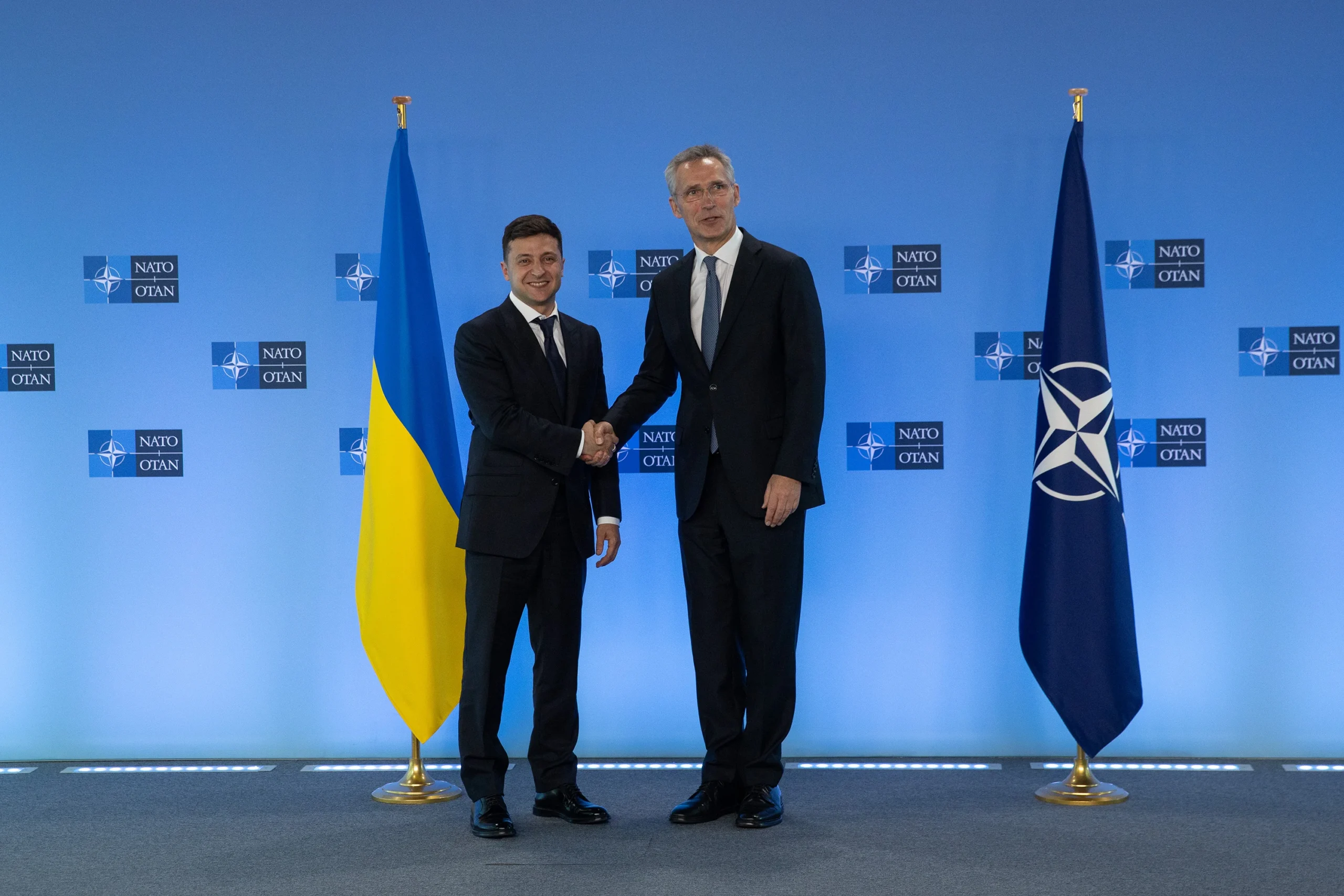Володимир Зеленський тисне руку Єнсу Столтенбергу перед прапорами України та НАТО.