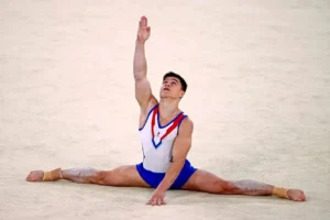 Російський гімнаст у формі з триколором виконує шпагат на змаганнях