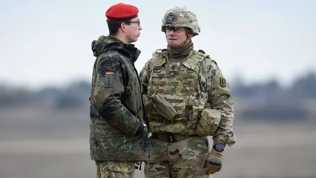 Німецький солдат у червоній беретці бесідує з американським військовим на тлі виведення контингенту США