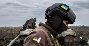 Боєць ЗСУ в касці з прапором біля знищеного танка ворога на полі.