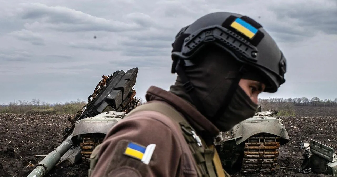 Боєць ЗСУ в касці з прапором біля знищеного танка ворога на полі.