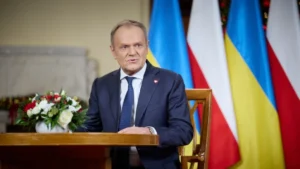Дональд Туск за трибуною на тлі прапорів України та Польщі
