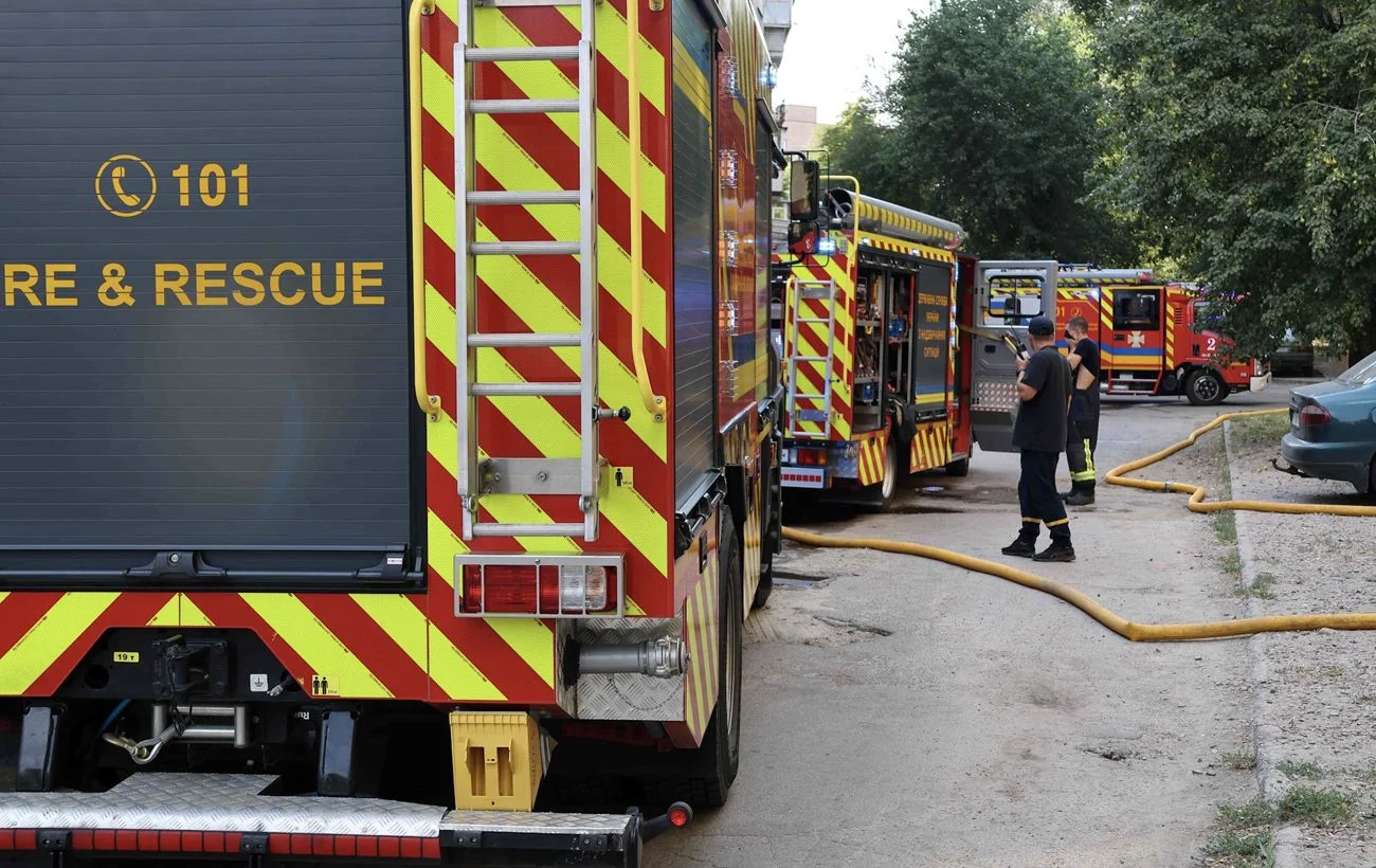 Пожежні машини з написом FIRE & RESCUE та рятувальники з рукавами на вулиці