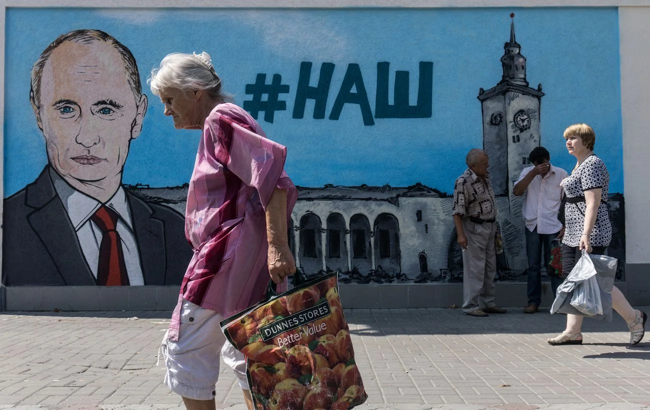Літня жінка з сумкою проходить повз мурал Путіна з написом #НАШ