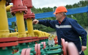 Працівник у касці регулює вентиль на жовто-червоних газових трубах